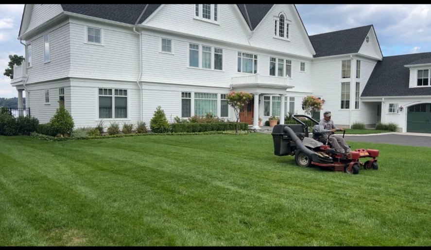 Freshly striped lawn being mowed in front of a large white residential home